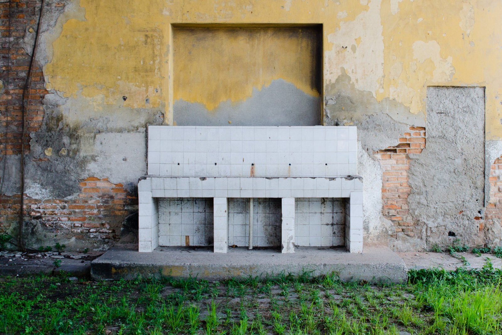 Worn plaster revealing brickwork behind a pale bench