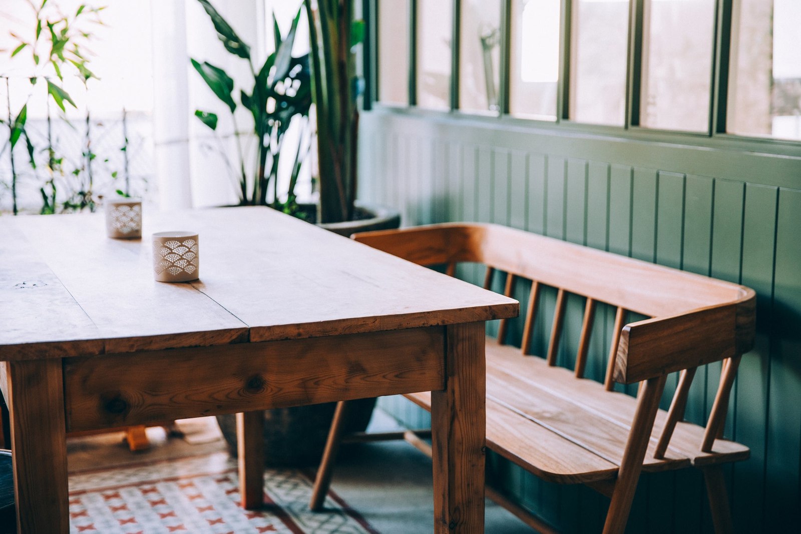 Wooden table and green bench seating beside bright windows